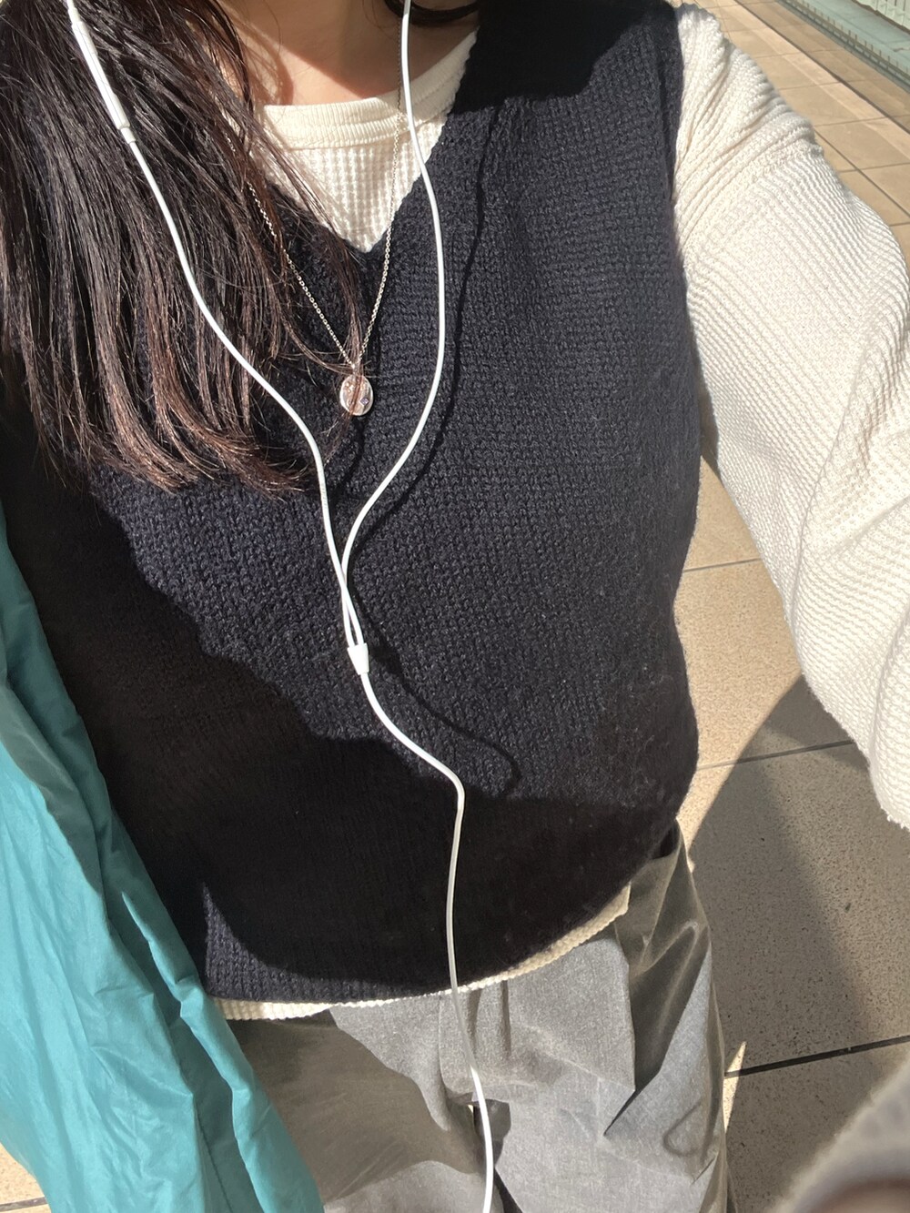 ブルー系のベスト、グレー系のスラックス、グリーン系のトートバッグを着用したレディースの秋コーディネートの2枚目の写真