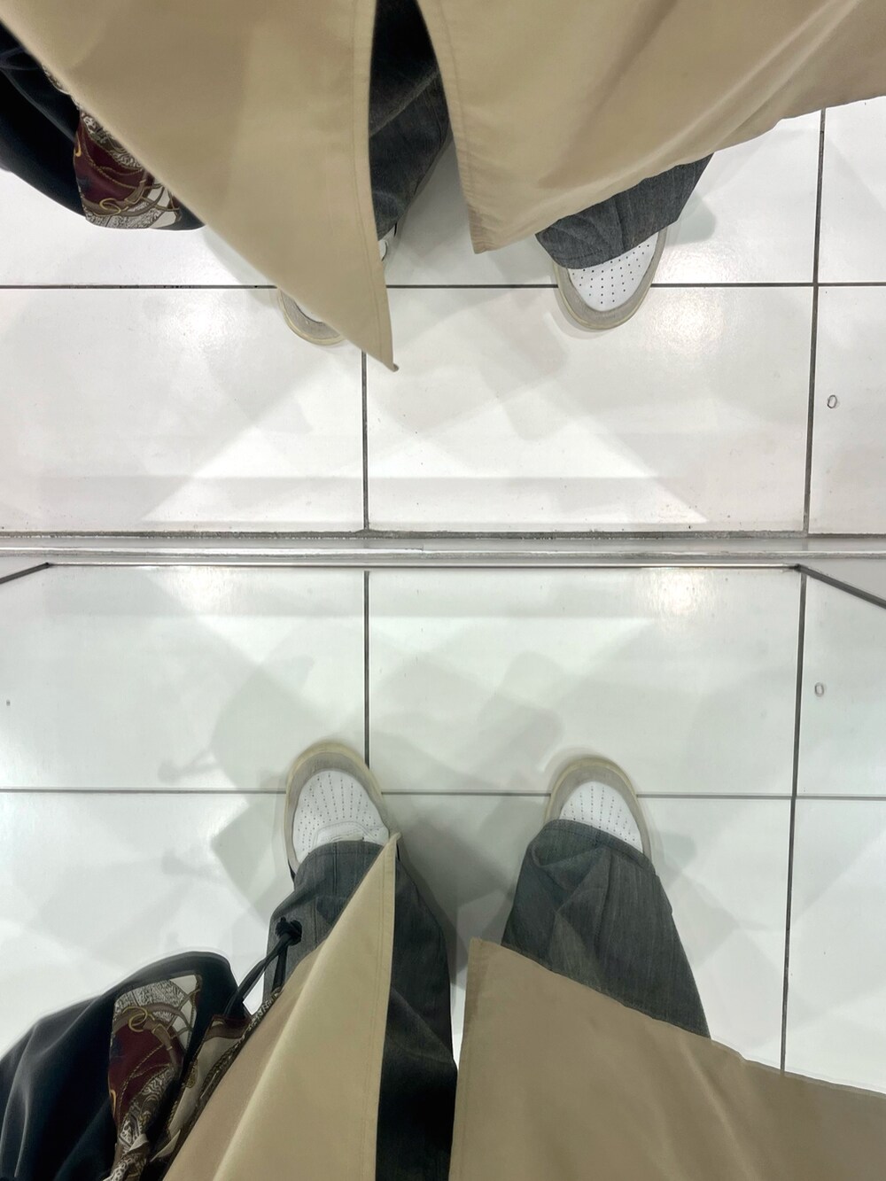 ベージュ系のトレンチコート、グレー系のスラックス、ブラック系のショルダーバッグを着用したメンズの春コーディネートの5枚目の写真