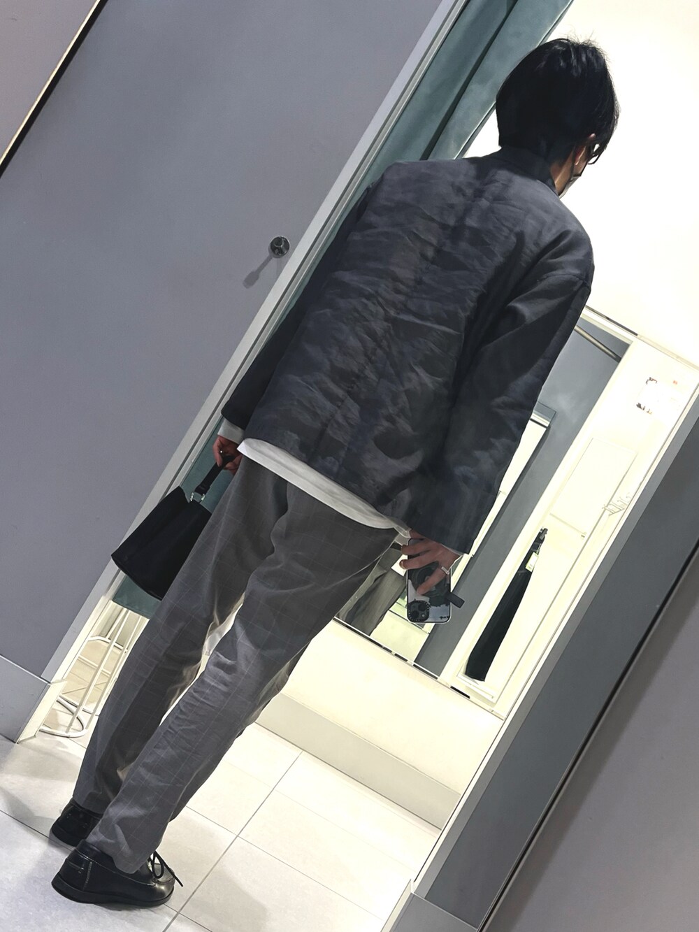 グレー系のスラックス、ブラック系のローファー、ブラック系のショルダーバッグを着用したメンズの春コーディネートの2枚目の写真