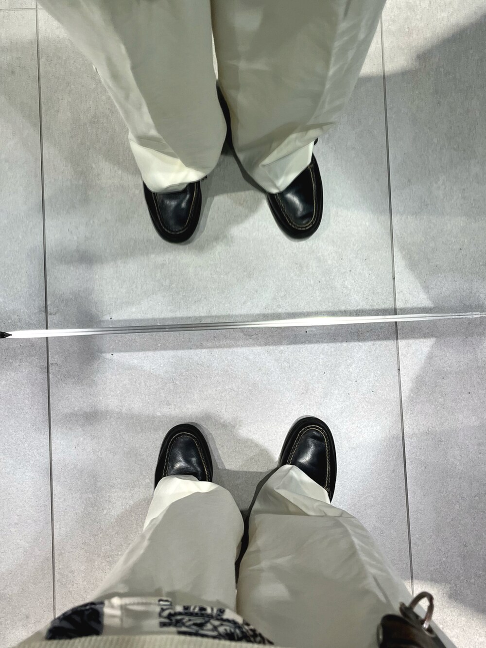 ブラック系のローファー、ホワイト系のスラックス、ベージュ系のベストを着用したメンズの秋コーディネートの5枚目の写真