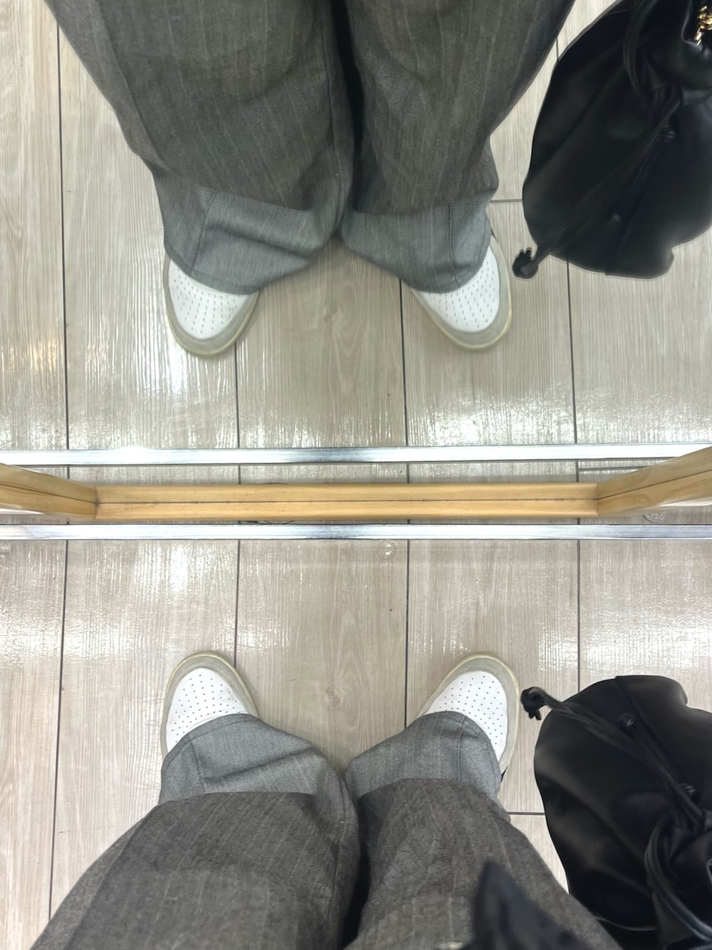 グレー系のスラックス、ブラック系のショルダーバッグ、ホワイト系のスニーカーを着用したメンズの冬コーディネートの5枚目の写真