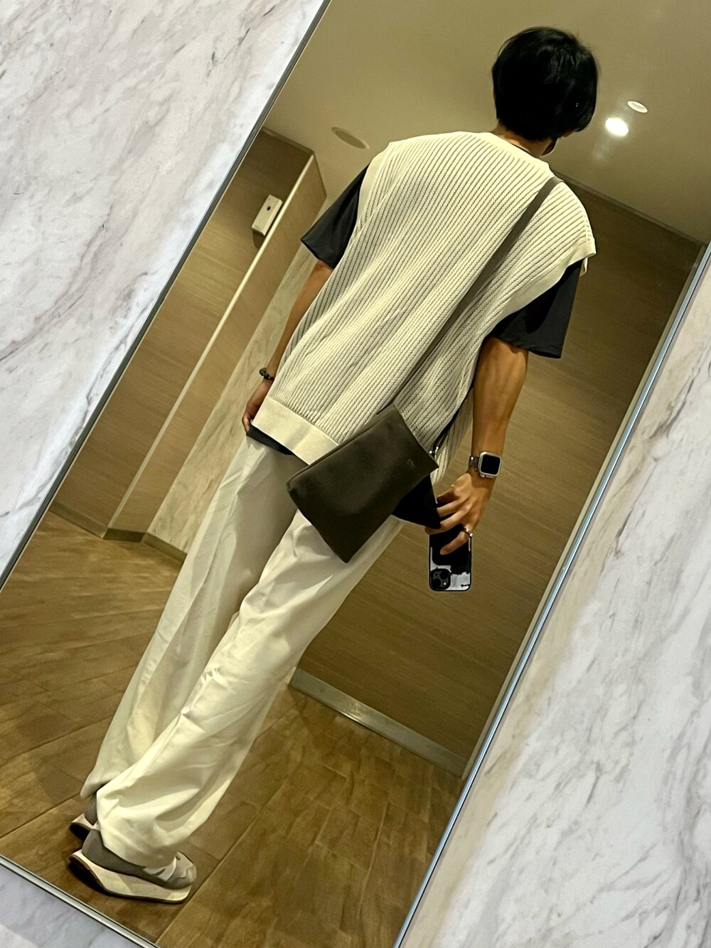 グレー系のスニーカー、ベージュ系のベスト、グレー系のショルダーバッグを着用したメンズの秋コーディネートの2枚目の写真