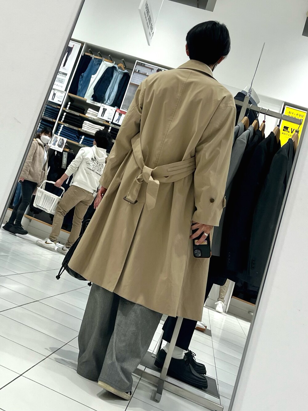 ベージュ系のトレンチコート、グレー系のスラックス、ブラック系のショルダーバッグを着用したメンズの春コーディネートの2枚目の写真