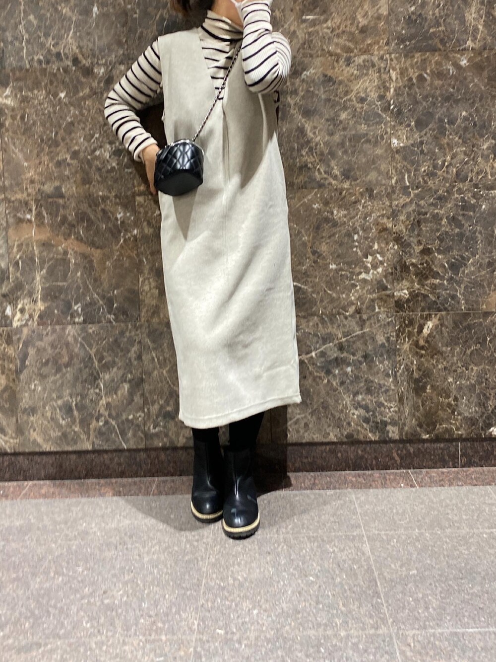 ホワイト系のジャンパースカート、ブラック系のバッグ、ベージュ系のニット/セーターを着用したレディースの冬コーディネートの2枚目の写真