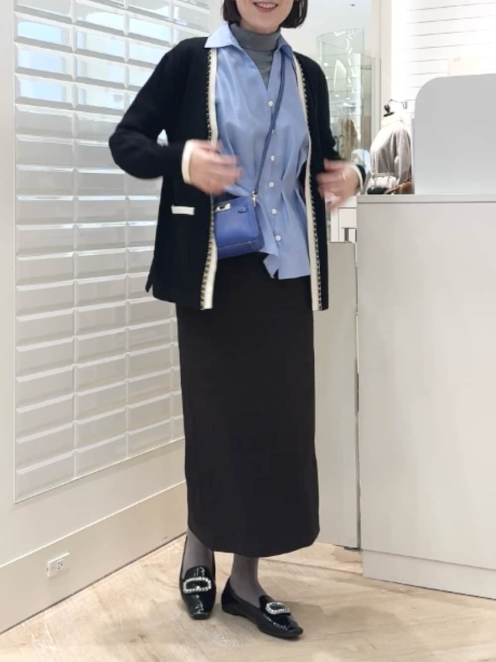 グレー系のニット/セーター、ベージュ系のスカート、ブルー系のショルダーバッグを着用したレディースの秋コーディネートの4枚目の写真