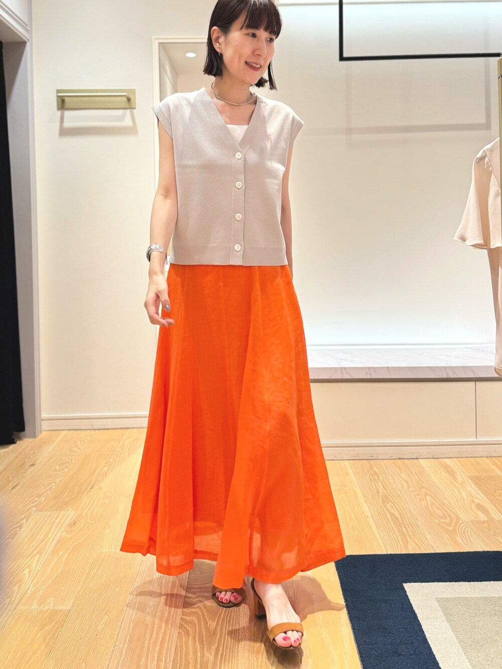 ベージュ系のベスト、ホワイト系のタンクトップ、オレンジ系のスカートを着用したレディースの夏コーディネートの9枚目の写真