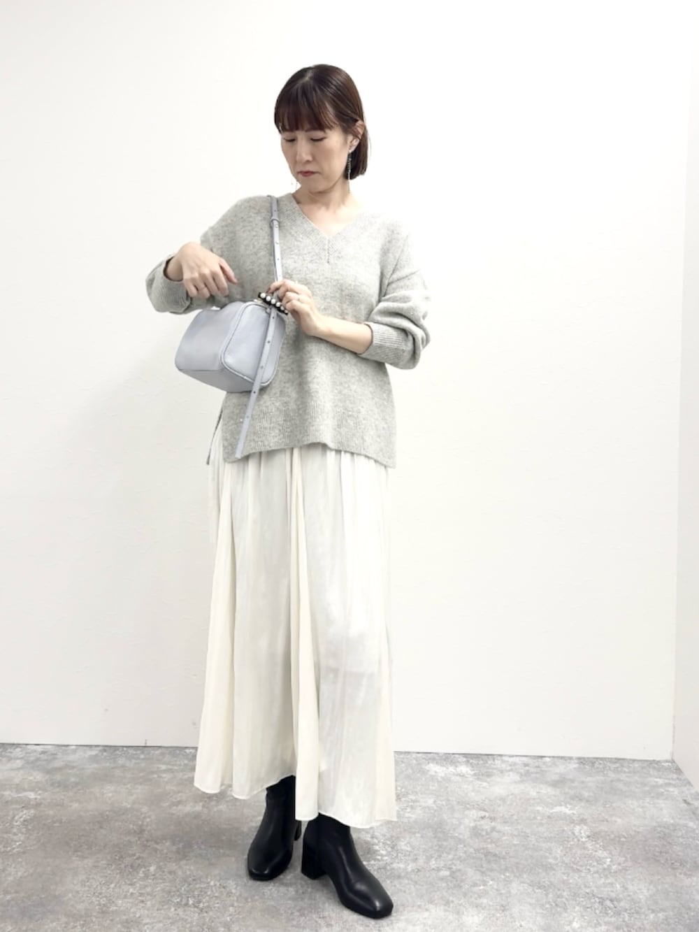 グレー系のニット/セーター、ブルー系のショルダーバッグ、ホワイト系のスカートを着用したレディースの冬コーディネートの3枚目の写真