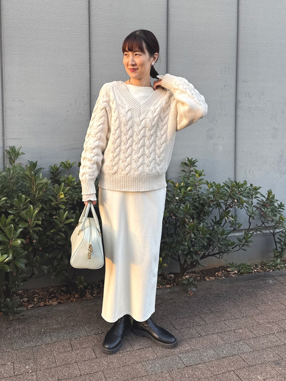 ホワイト系のニット/セーター、ホワイト系のTシャツ/カットソー、グリーン系のショルダーバッグを着用したレディースの冬コーディネートの2枚目の写真