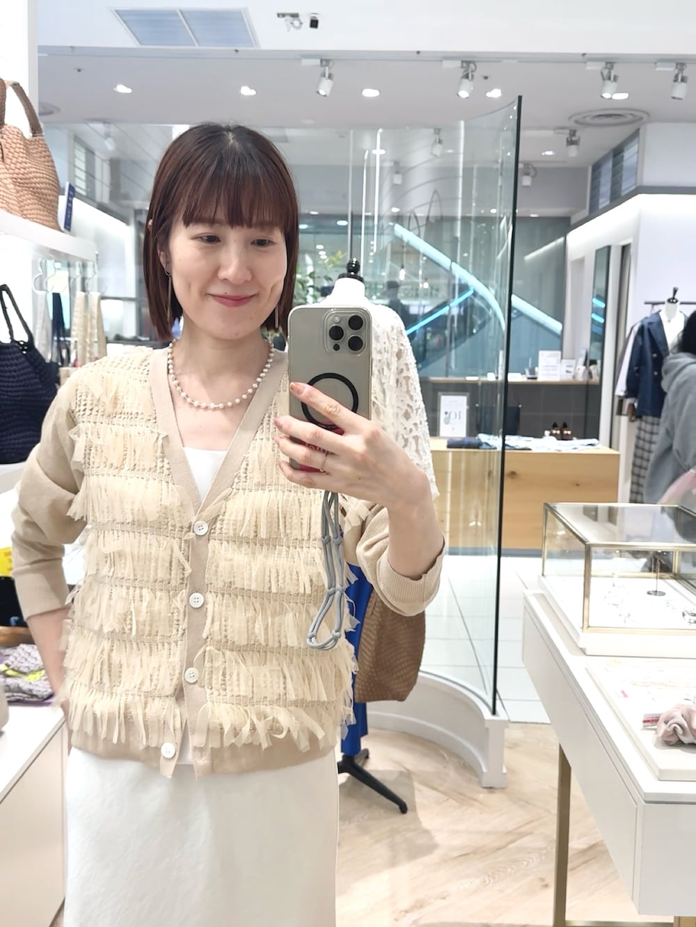 ホワイト系のスカート、ホワイト系のタンクトップ、ベージュ系のカーディガン/ボレロを着用したレディースの春コーディネートの3枚目の写真