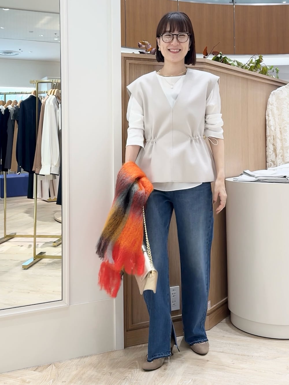 ブルー系のデニムパンツ、ベージュ系のベスト、ホワイト系のシャツ/ブラウスを着用したレディースの秋コーディネートの3枚目の写真