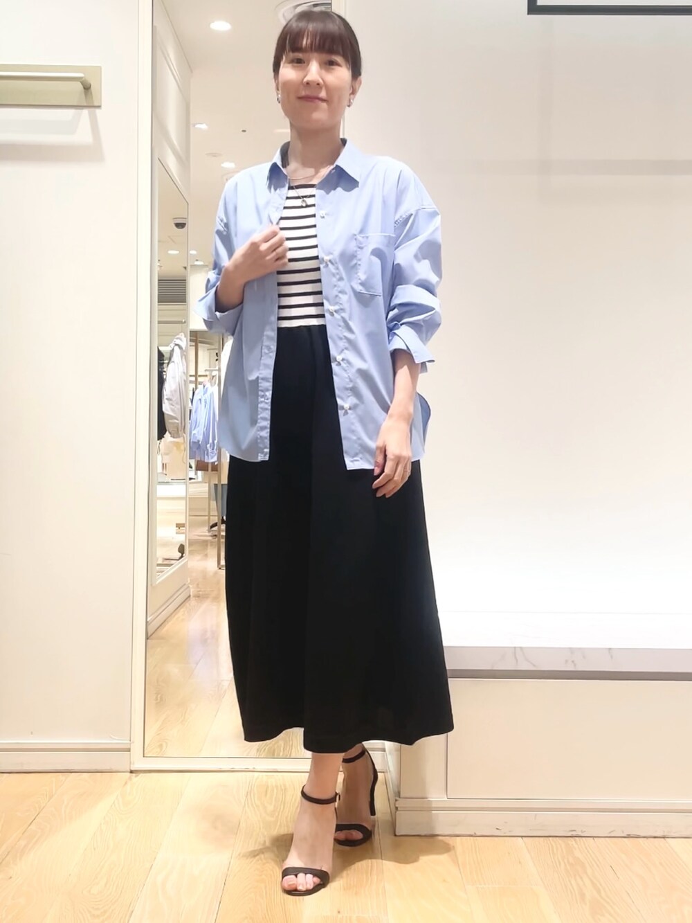 ブルー系のシャツ/ブラウス、ブラック系のワンピース、ゴールド系のイヤリングを着用したレディースの春コーディネートの2枚目の写真