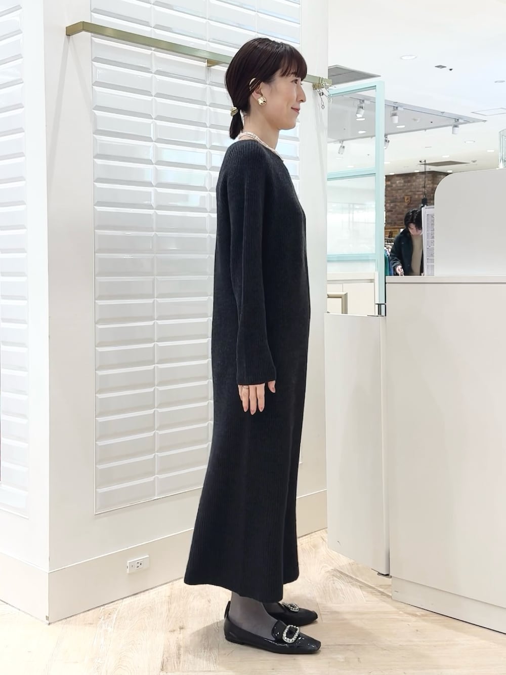 グレー系のワンピース、ゴールド系のイヤリング、ホワイト系のネックレスを着用したレディースの冬コーディネートの3枚目の写真