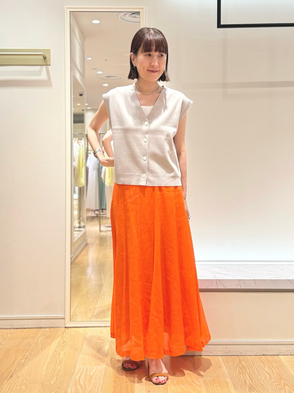 ベージュ系のベスト、ホワイト系のタンクトップ、オレンジ系のスカートを着用したレディースの夏コーディネートの2枚目の写真