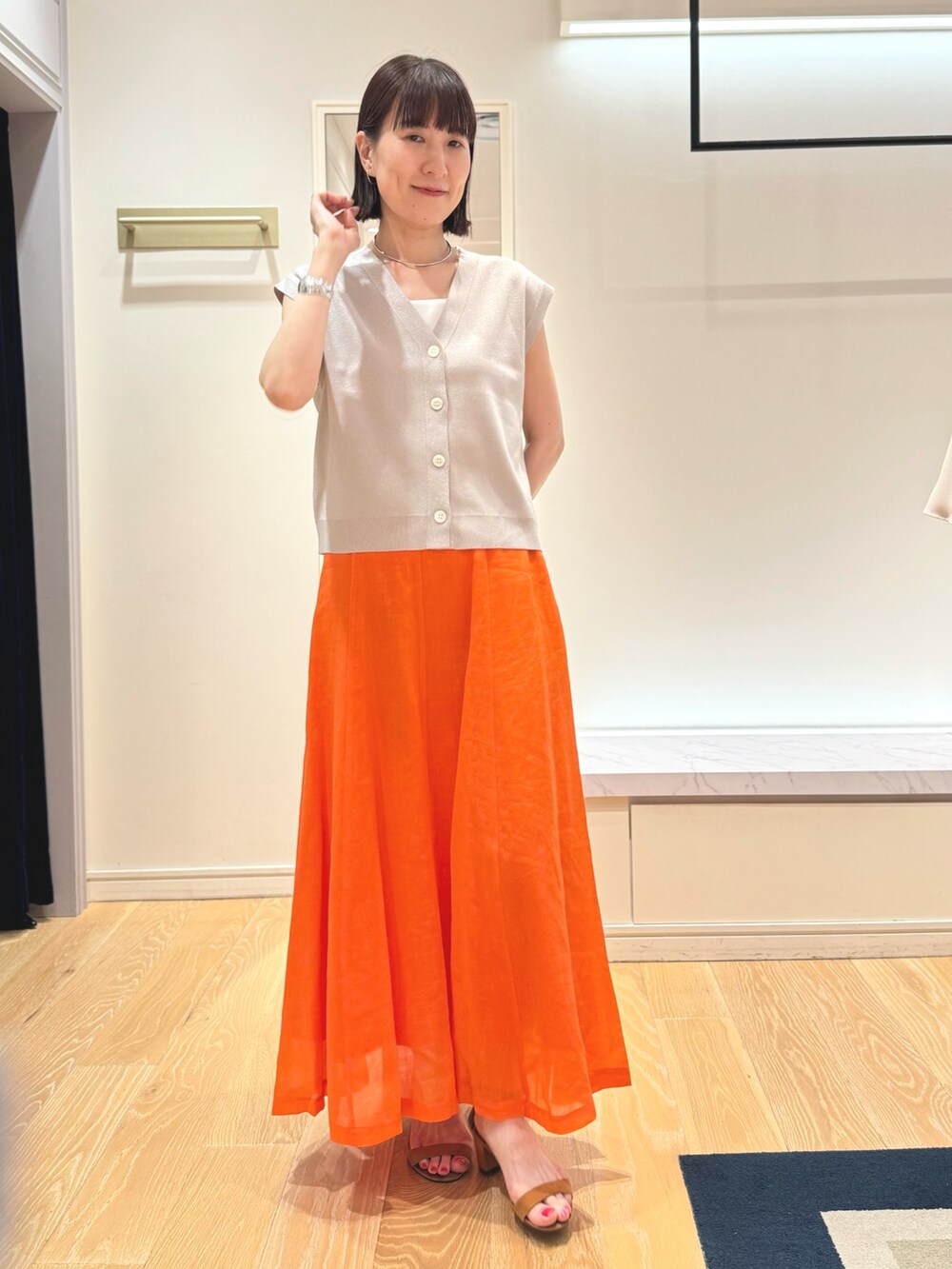ベージュ系のベスト、ホワイト系のタンクトップ、オレンジ系のスカートを着用したレディースの夏コーディネートの8枚目の写真