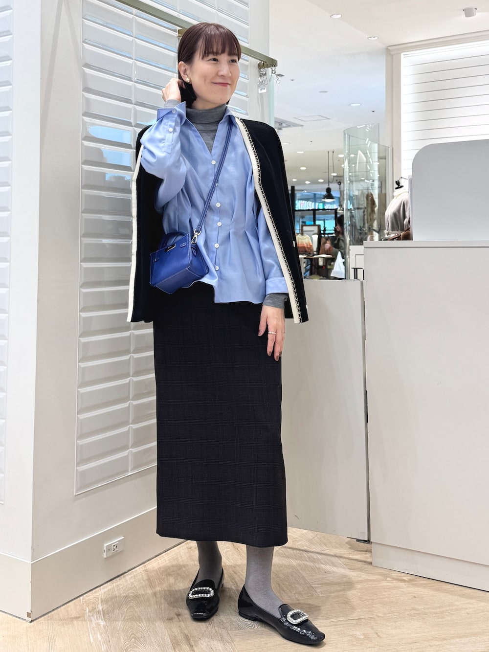 グレー系のニット/セーター、ベージュ系のスカート、ブルー系のショルダーバッグを着用したレディースの秋コーディネートの2枚目の写真