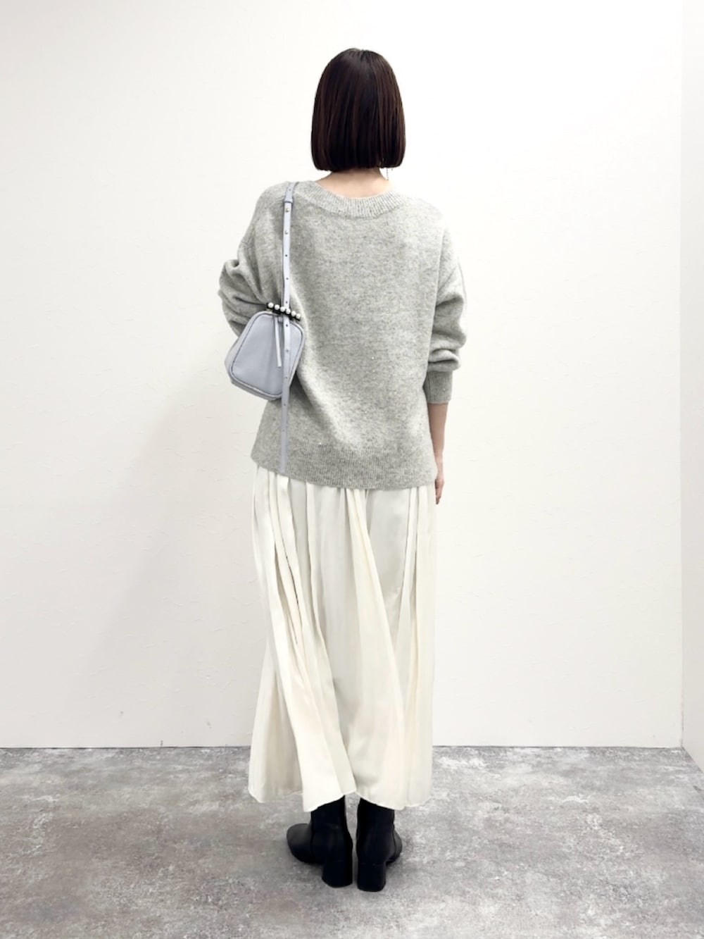 グレー系のニット/セーター、ブルー系のショルダーバッグ、ホワイト系のスカートを着用したレディースの冬コーディネートの4枚目の写真