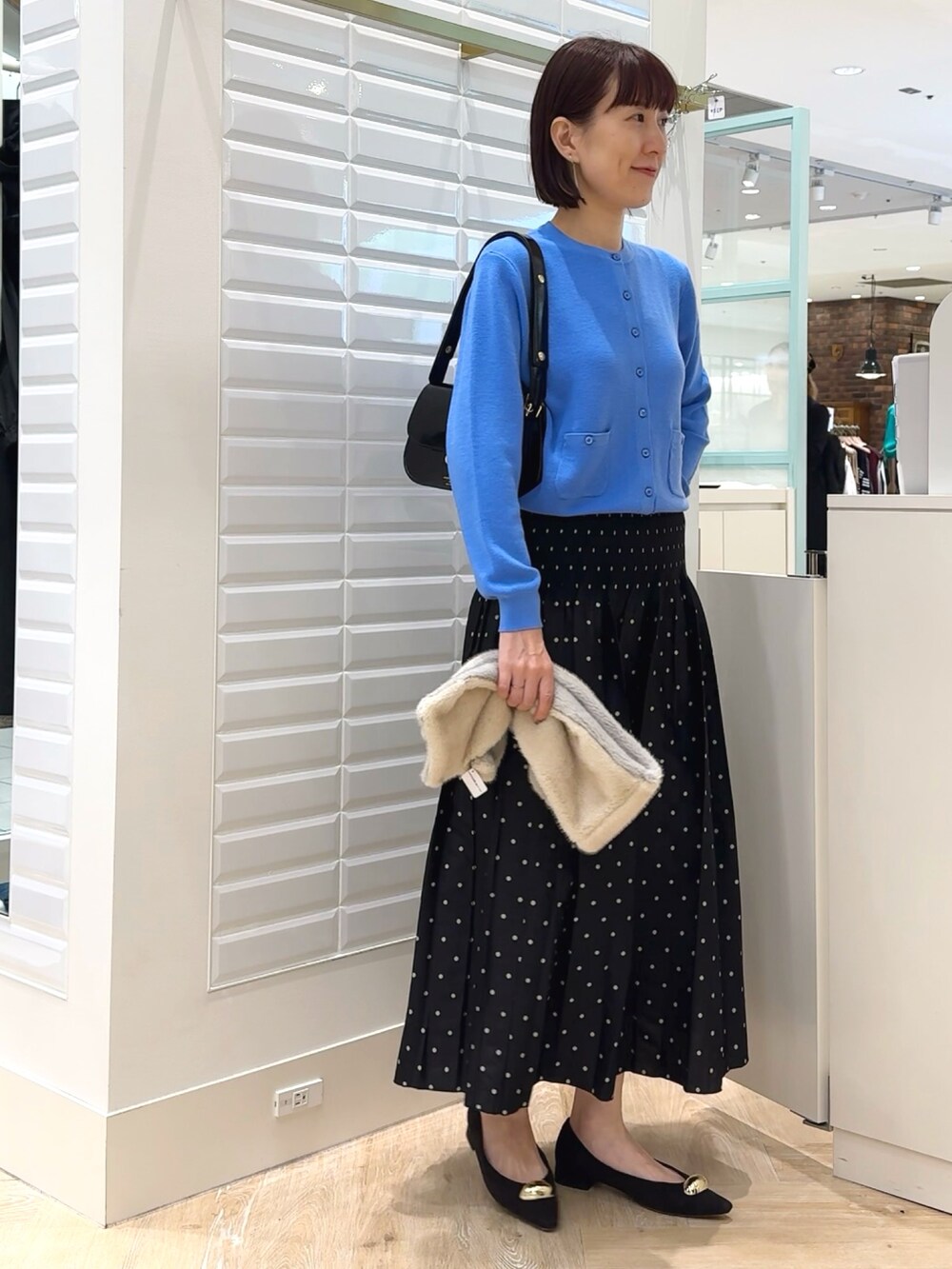 ブラック系のショルダーバッグ、ブルー系のカーディガン/ボレロ、ブラック系のスカートを着用したレディースの秋コーディネートの6枚目の写真