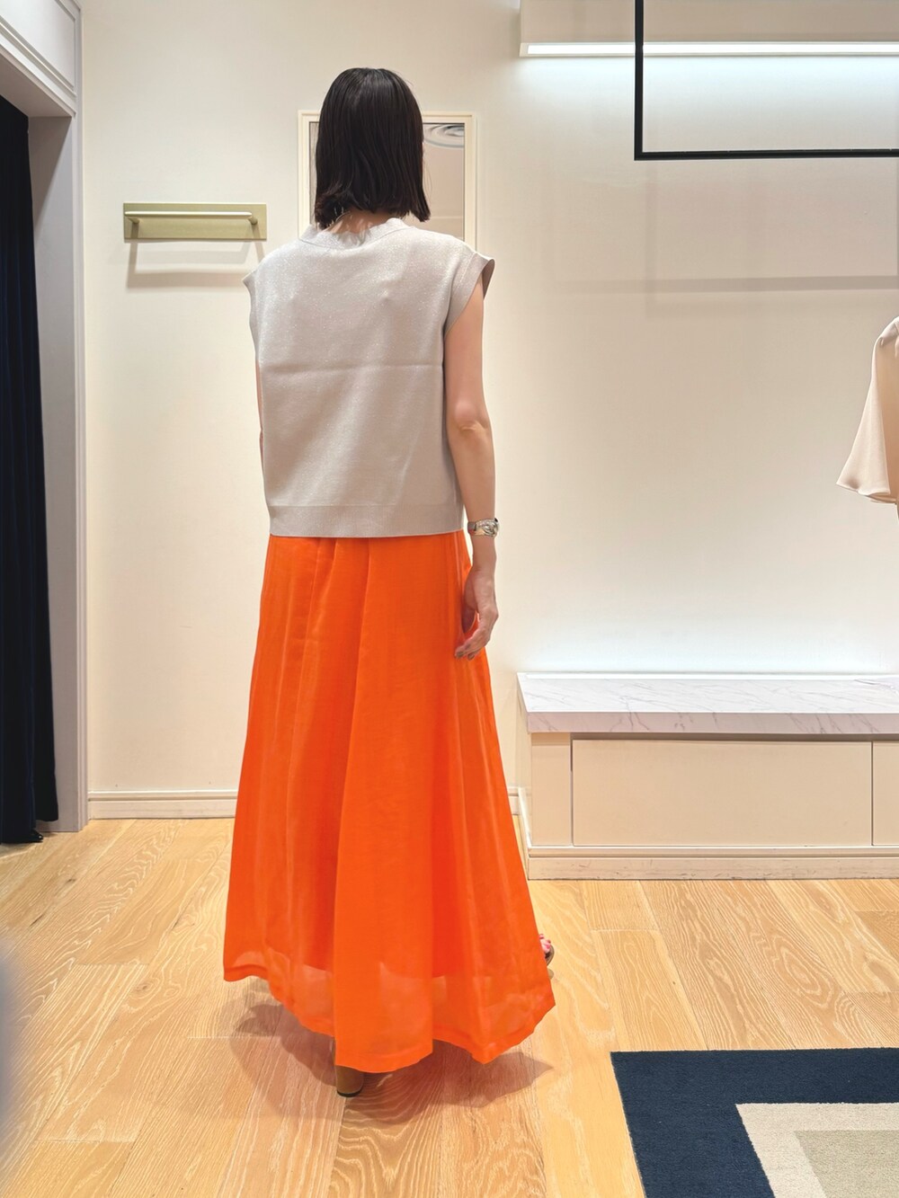 ベージュ系のベスト、ホワイト系のタンクトップ、オレンジ系のスカートを着用したレディースの夏コーディネートの5枚目の写真