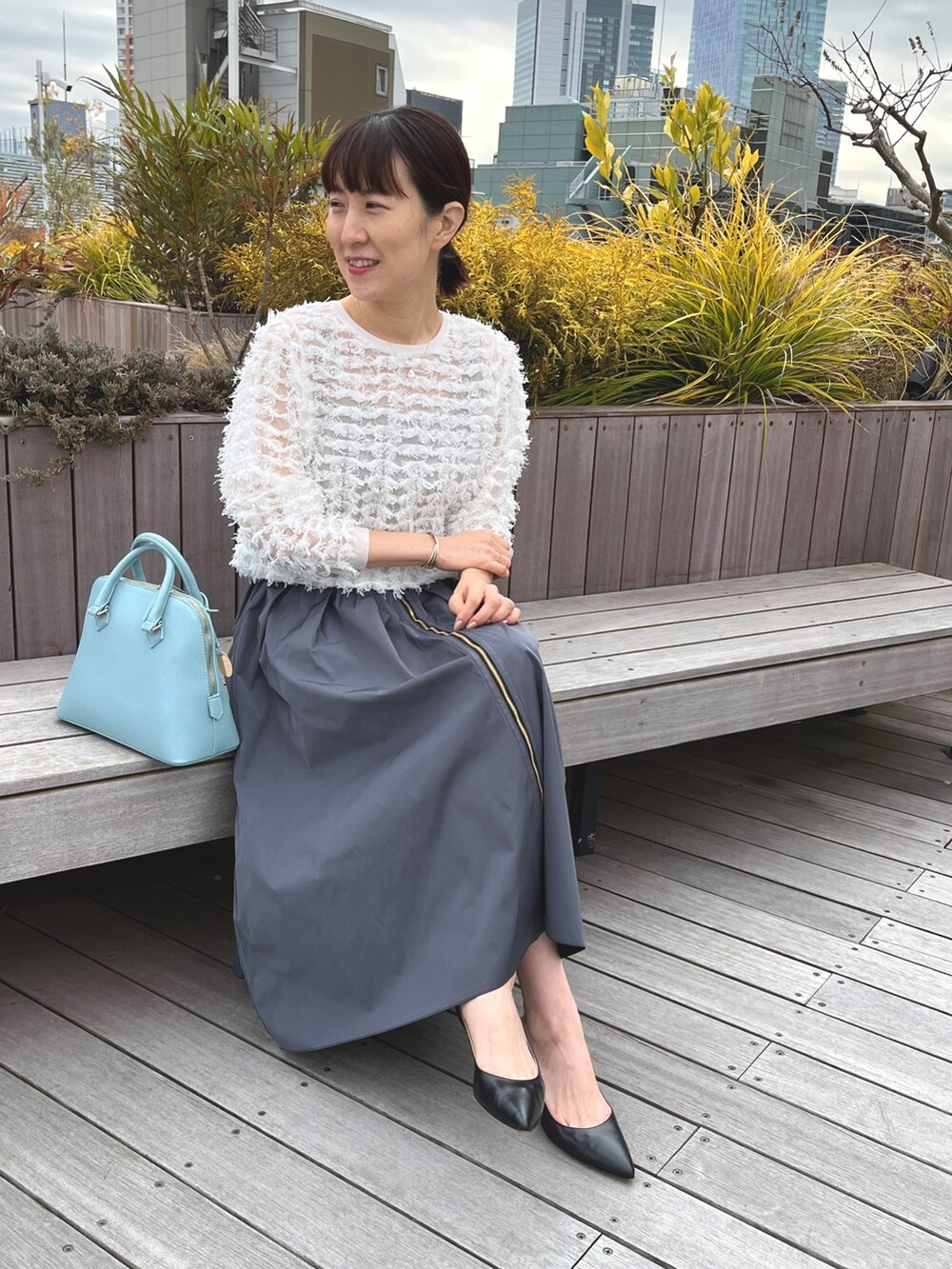 ブルー系のボストンバッグ、ブラック系のパンプス、グレー系のスカートを着用したレディースの冬コーディネートの4枚目の写真