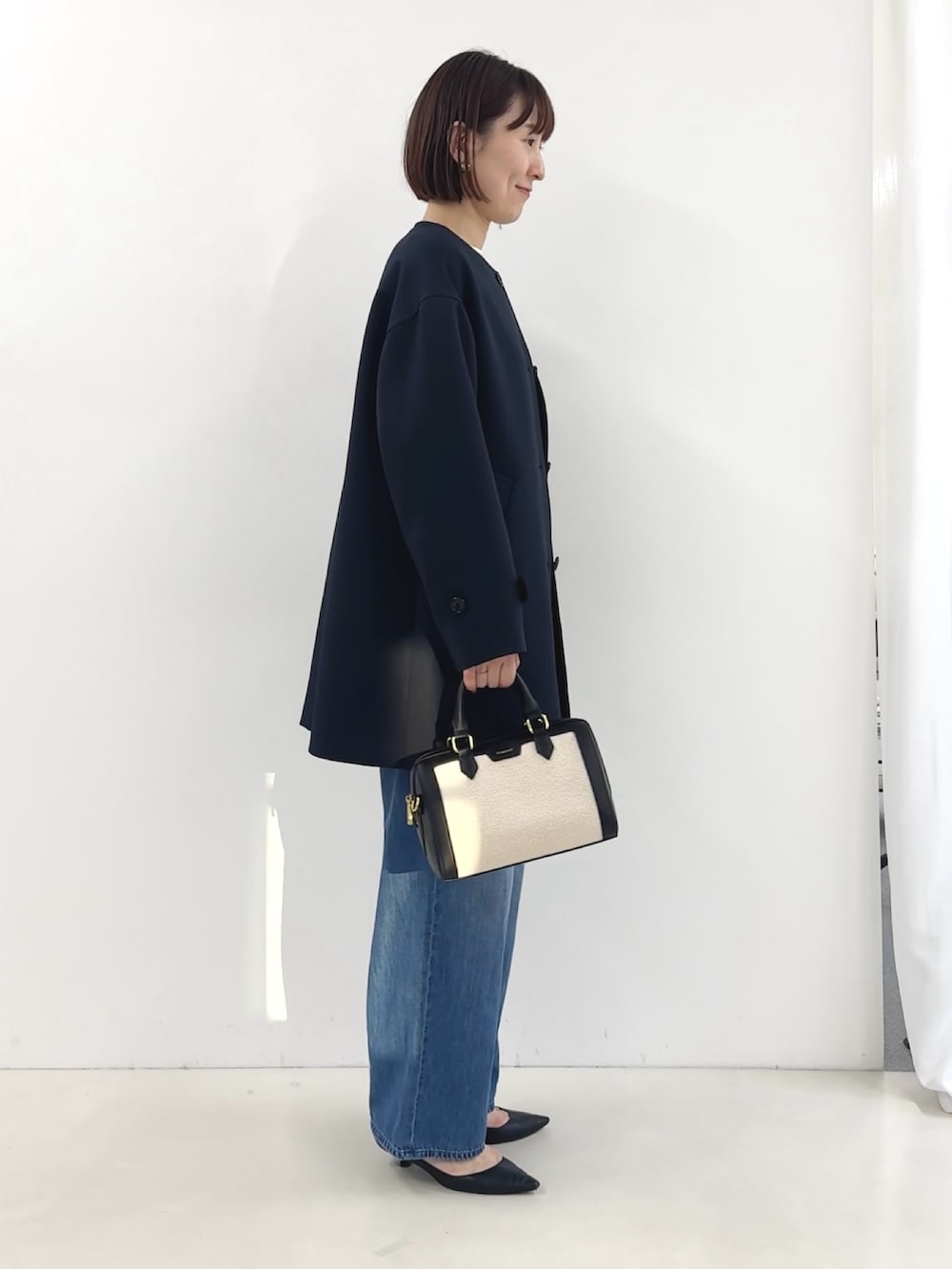 ブラック系のボストンバッグ、ホワイト系のTシャツ/カットソー、ブルー系のステンカラーコートを着用したレディースの冬コーディネートの5枚目の写真