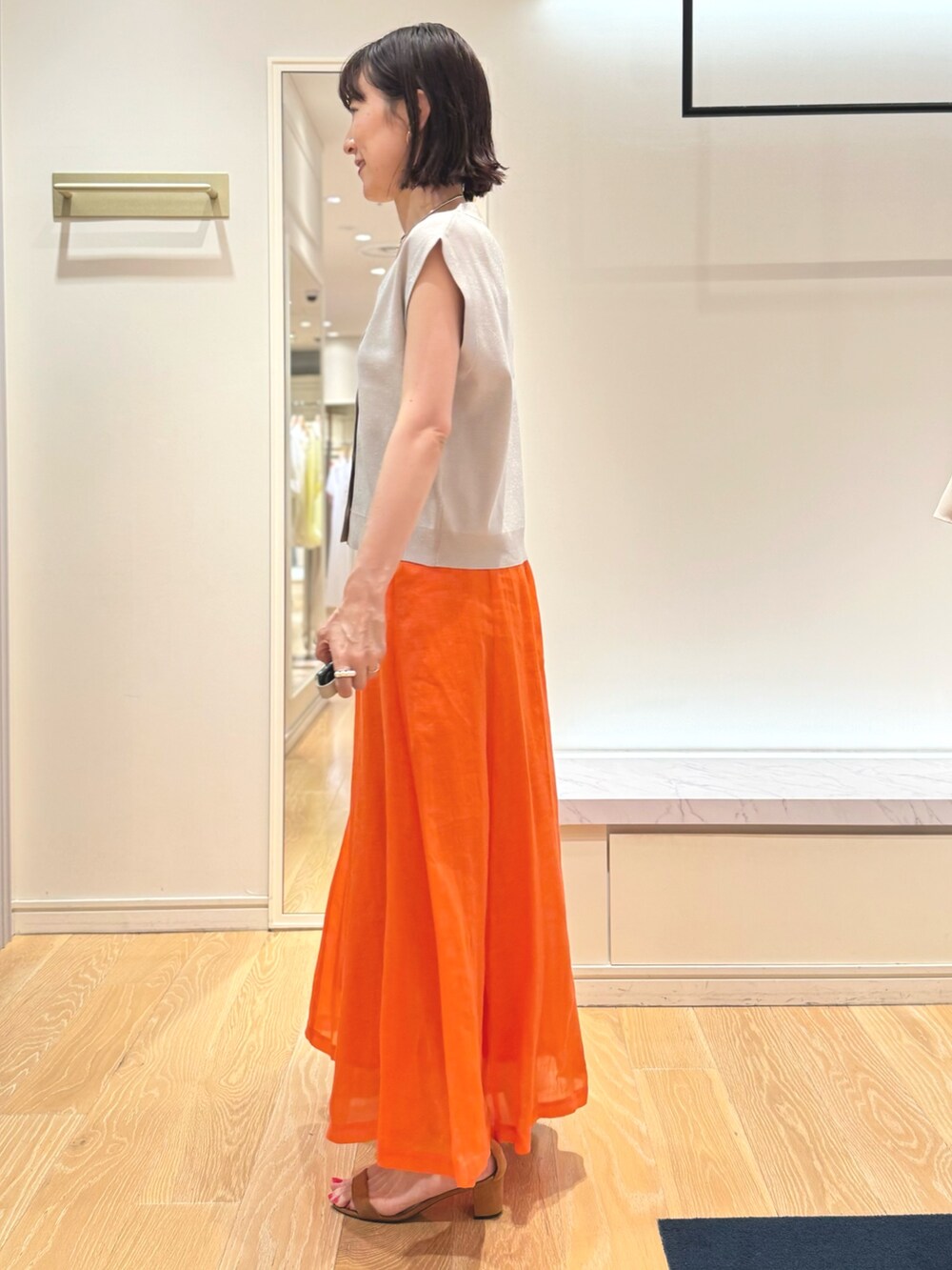 ベージュ系のベスト、ホワイト系のタンクトップ、オレンジ系のスカートを着用したレディースの夏コーディネートの3枚目の写真