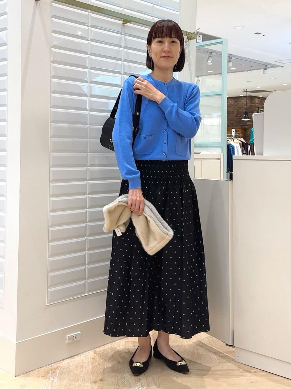 ブラック系のショルダーバッグ、ブルー系のカーディガン/ボレロ、ブラック系のスカートを着用したレディースの秋コーディネートの2枚目の写真