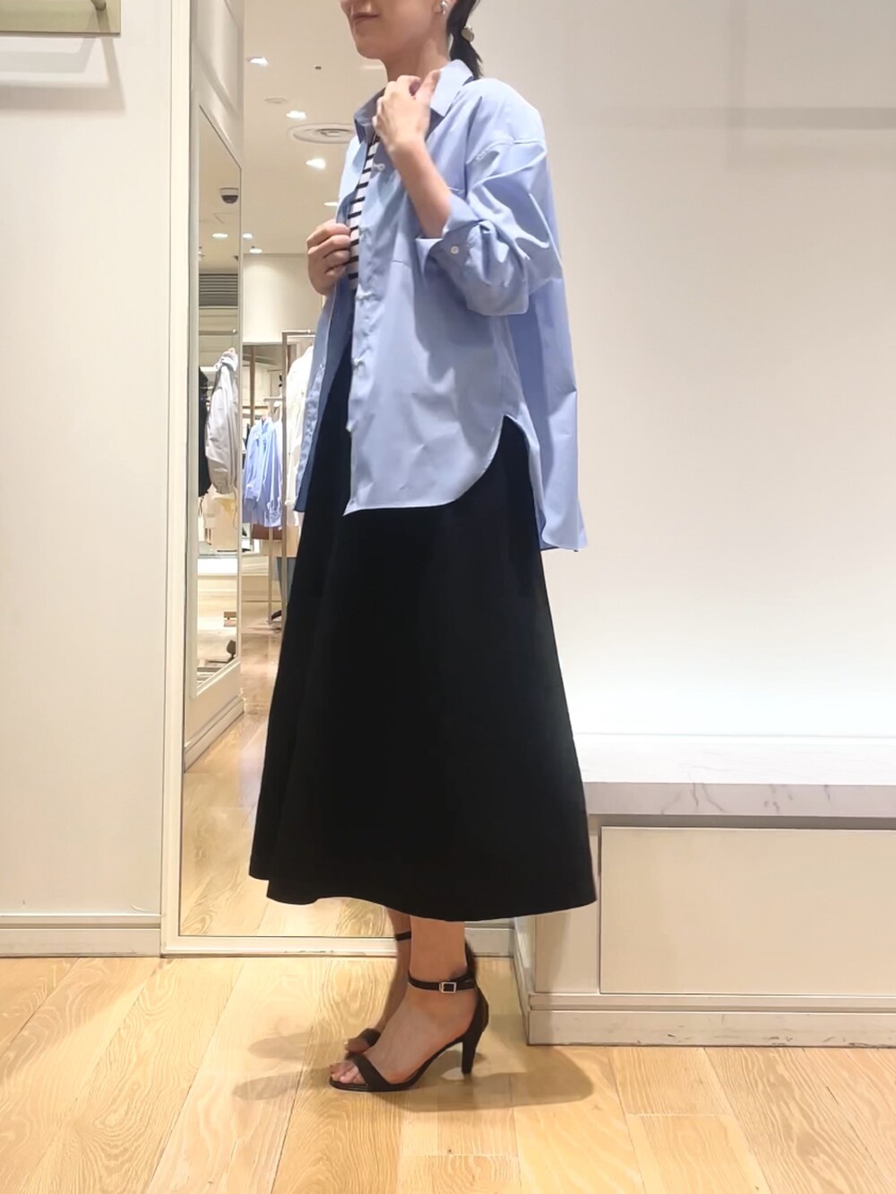 ブルー系のシャツ/ブラウス、ブラック系のワンピース、ゴールド系のイヤリングを着用したレディースの春コーディネートの5枚目の写真