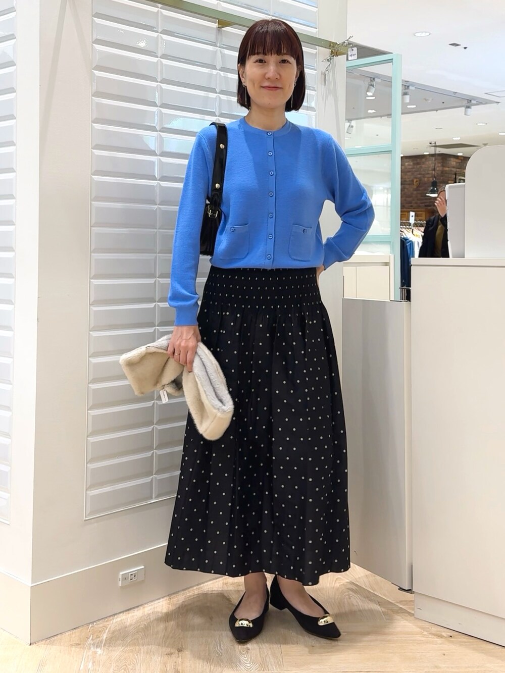 ブラック系のショルダーバッグ、ブルー系のカーディガン/ボレロ、ブラック系のスカートを着用したレディースの秋コーディネートの5枚目の写真
