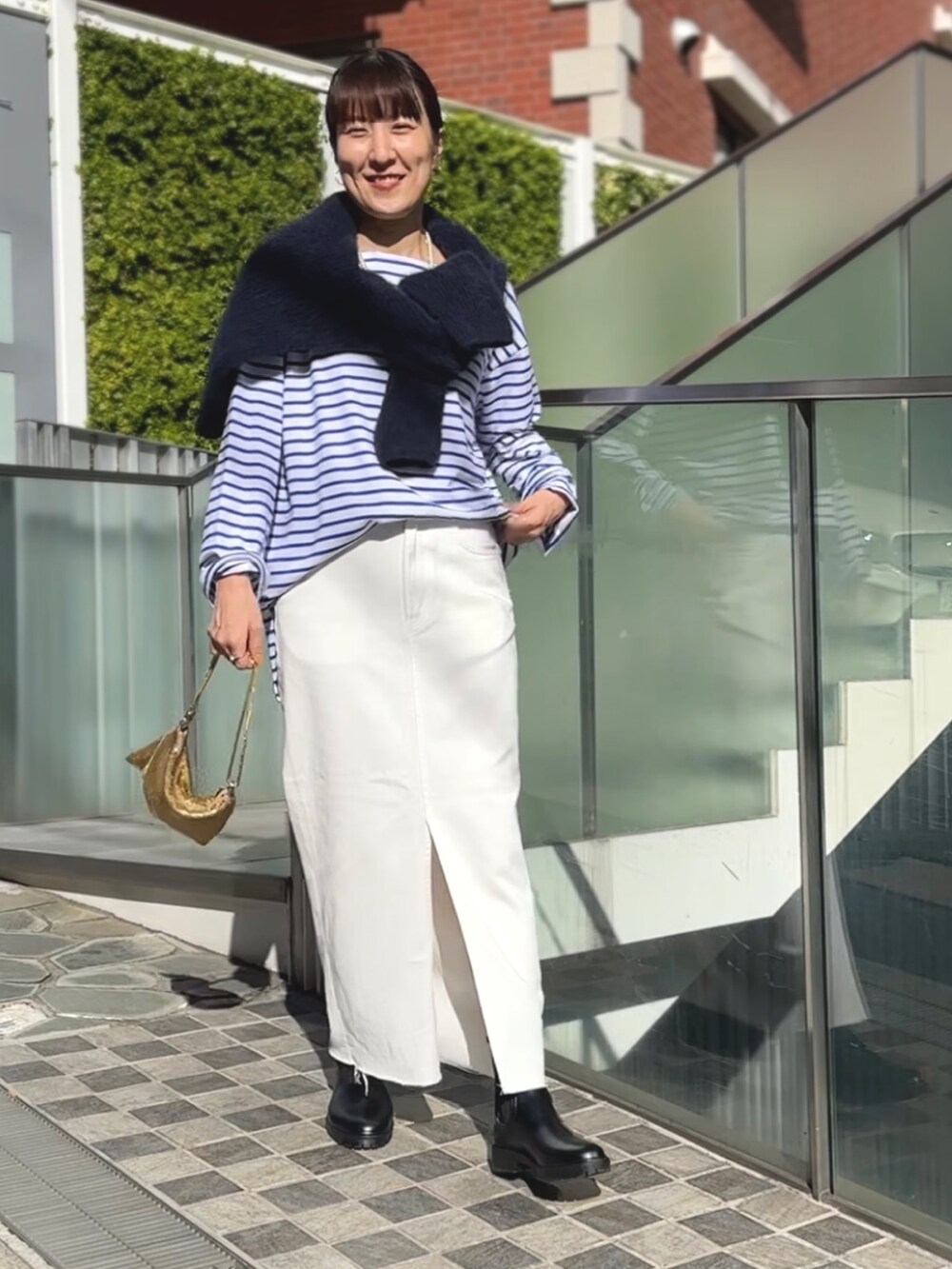 ゴールド系のクラッチバッグ、ブラック系のブーツ、ホワイト系のデニムスカートを着用したレディースの冬コーディネートの6枚目の写真