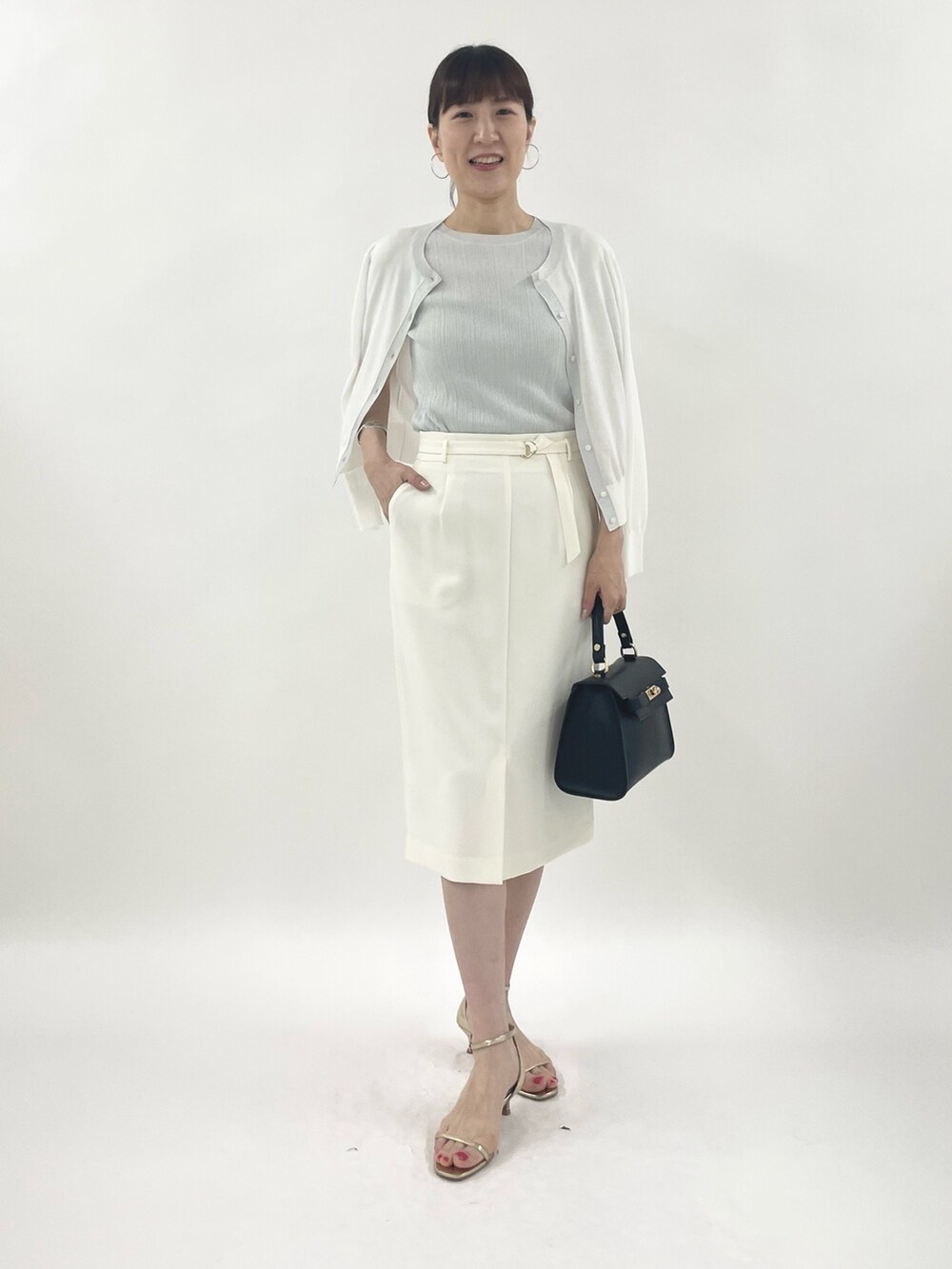 ゴールド系のサンダル、ブラック系のショルダーバッグ、シルバー系のニット/セーターを着用したレディースの春コーディネートの2枚目の写真