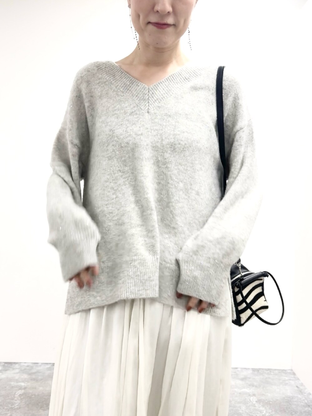 グレー系のニット/セーター、ブルー系のショルダーバッグ、ホワイト系のスカートを着用したレディースの冬コーディネートの6枚目の写真