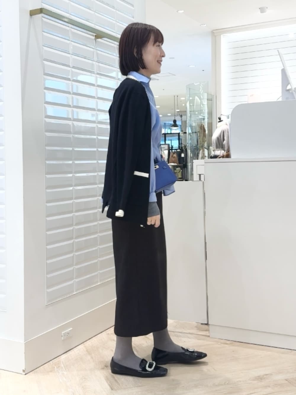 グレー系のニット/セーター、ベージュ系のスカート、ブルー系のショルダーバッグを着用したレディースの秋コーディネートの3枚目の写真