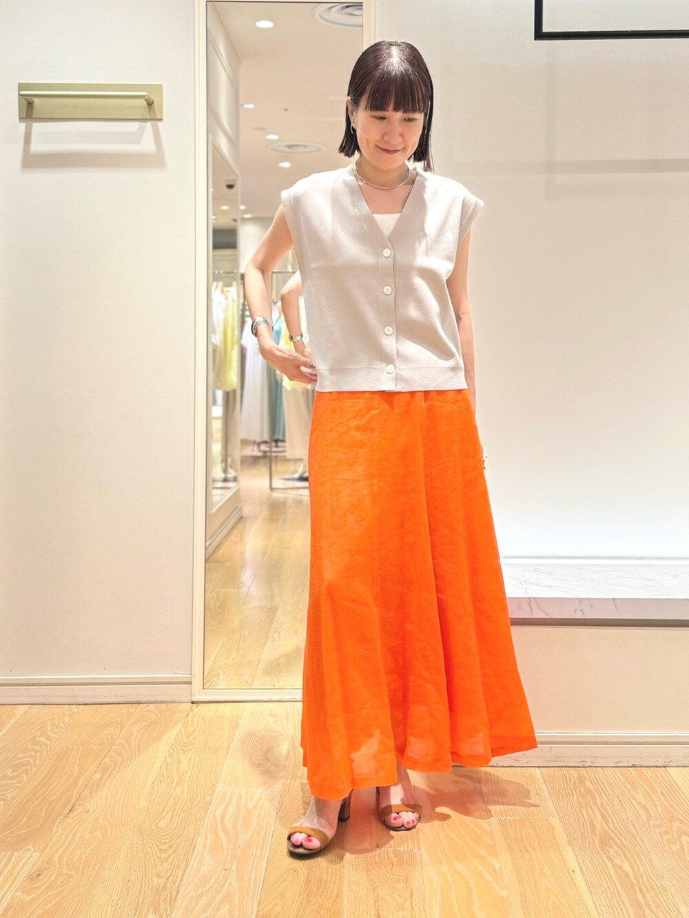 ベージュ系のベスト、ホワイト系のタンクトップ、オレンジ系のスカートを着用したレディースの夏コーディネートの6枚目の写真