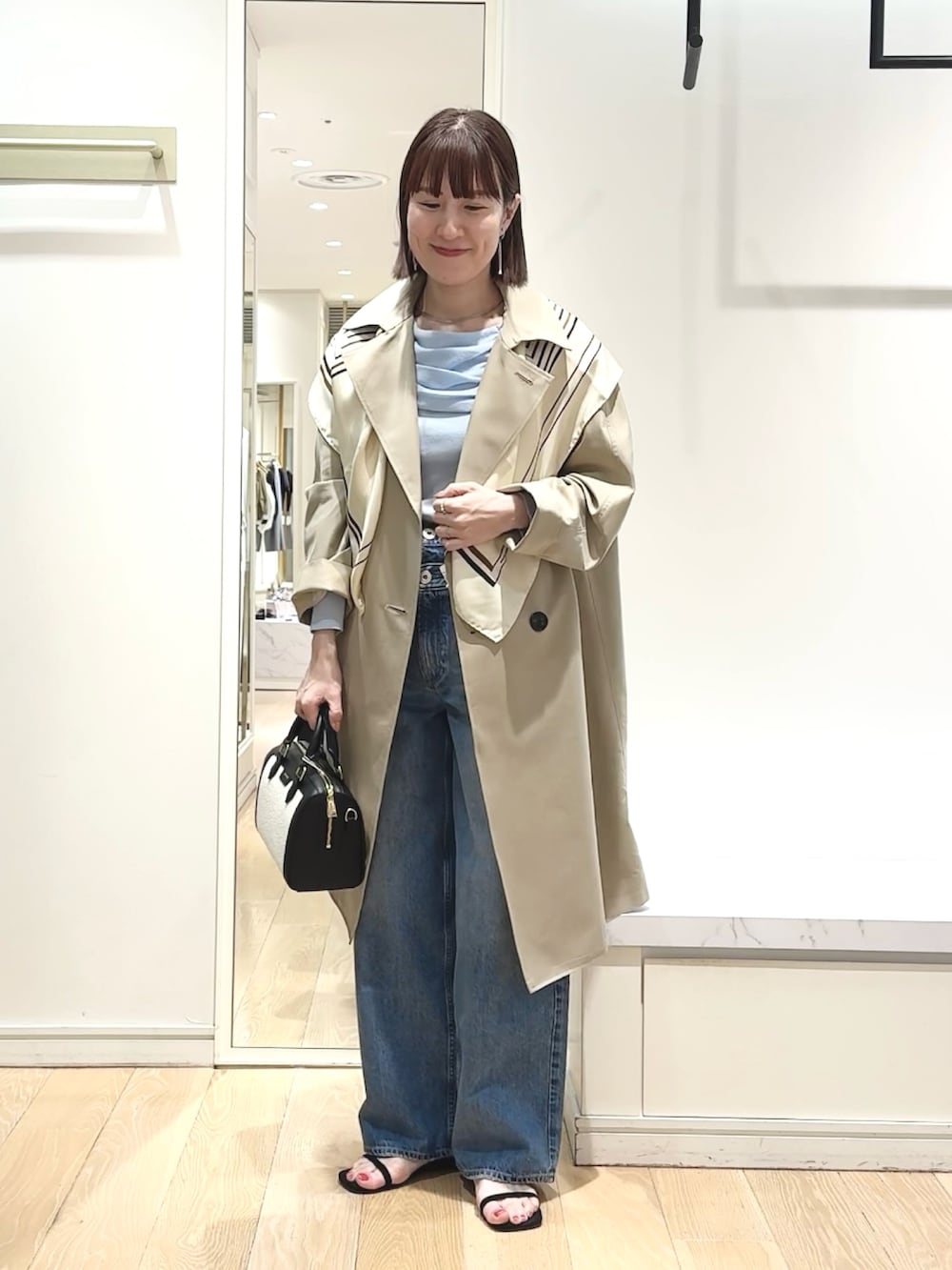 ブラック系のボストンバッグ、ブルー系のニット/セーター、ベージュ系のトレンチコートを着用したレディースの春コーディネートの6枚目の写真