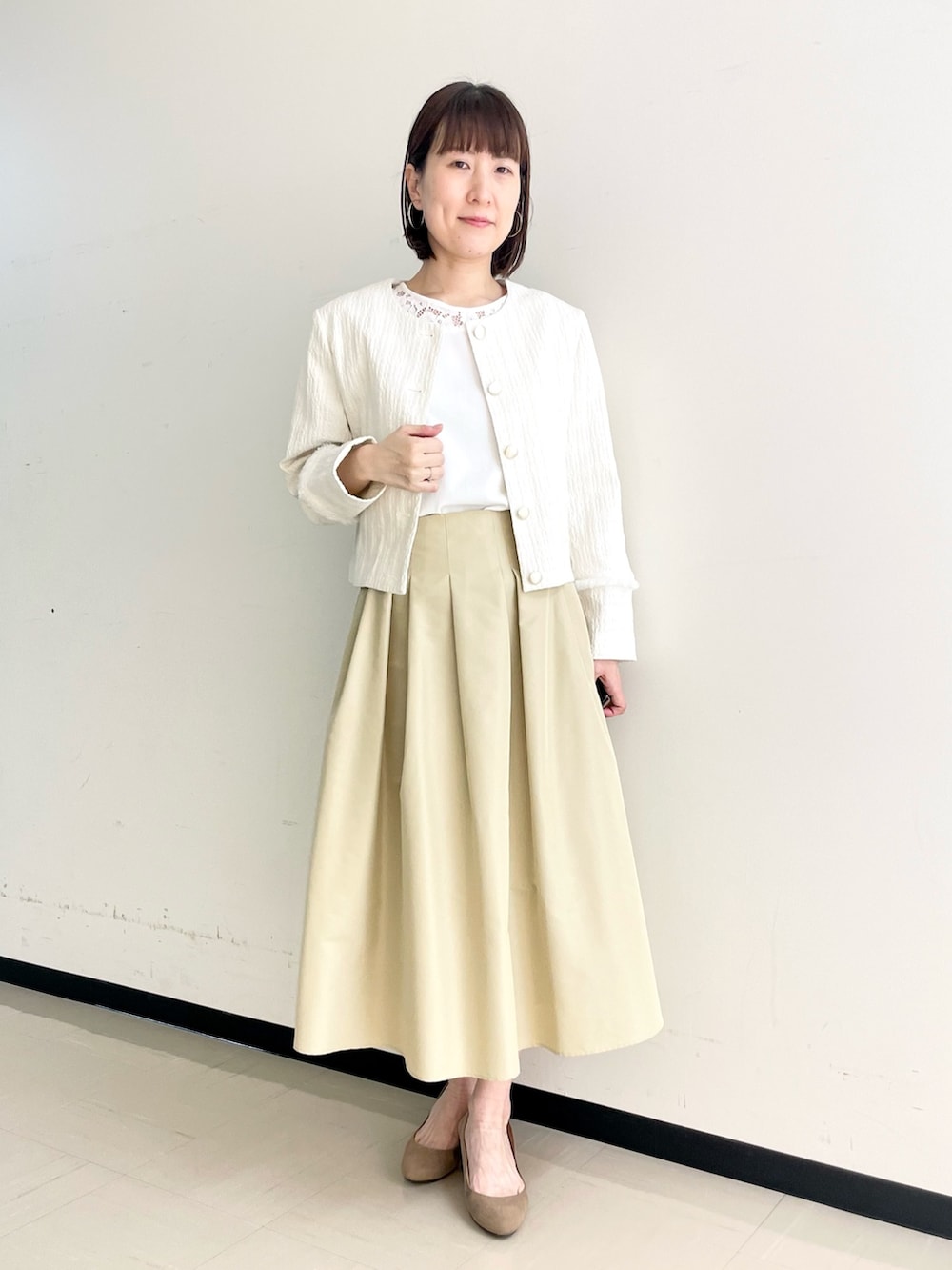 ベージュ系のスカート、ホワイト系のノーカラージャケット、ホワイト系のニット/セーターを着用したレディースの春コーディネートの2枚目の写真