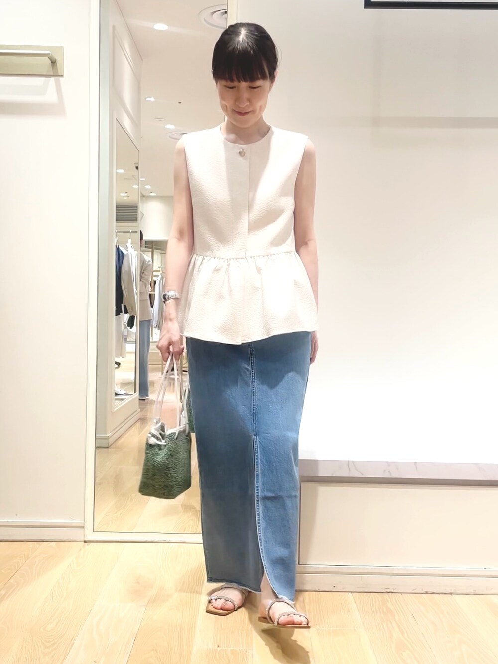 ホワイト系のベスト、グリーン系のショルダーバッグ、ブルー系のデニムスカートを着用したレディースの春コーディネートの3枚目の写真