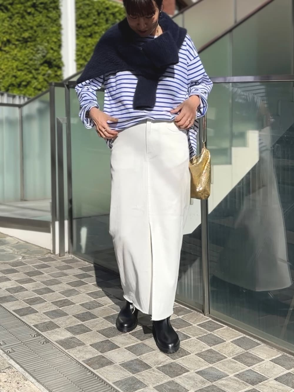 ゴールド系のクラッチバッグ、ブラック系のブーツ、ホワイト系のデニムスカートを着用したレディースの冬コーディネートの4枚目の写真