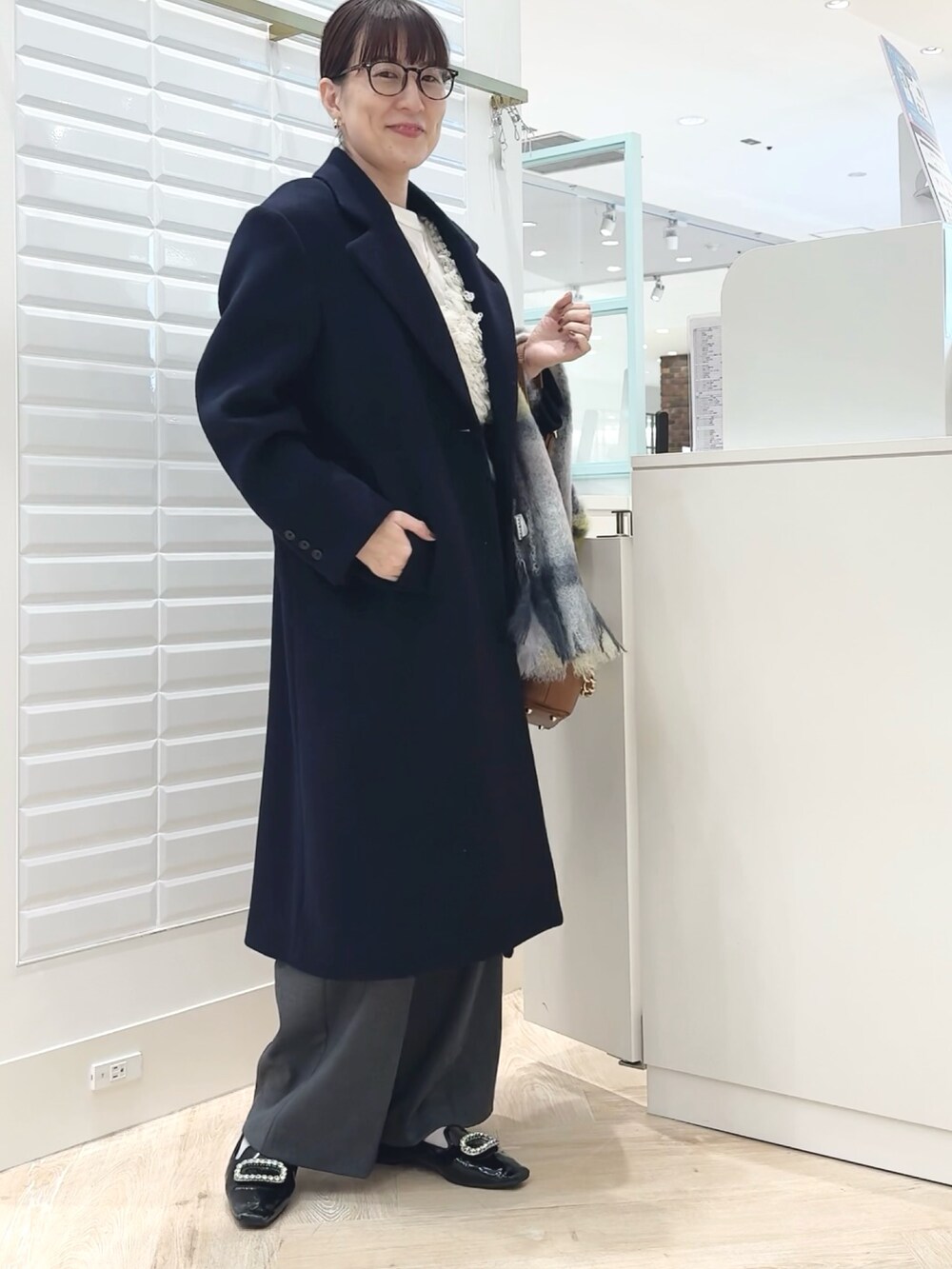 グレー系のその他パンツ、ブルー系のチェスターコート、ホワイト系のベストを着用したレディースの秋コーディネートの5枚目の写真