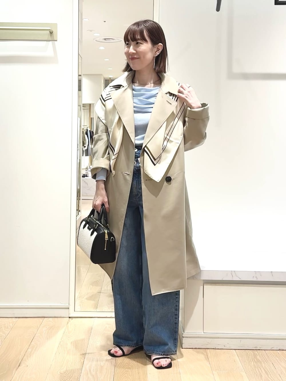 ブラック系のボストンバッグ、ブルー系のニット/セーター、ベージュ系のトレンチコートを着用したレディースの春コーディネートの3枚目の写真