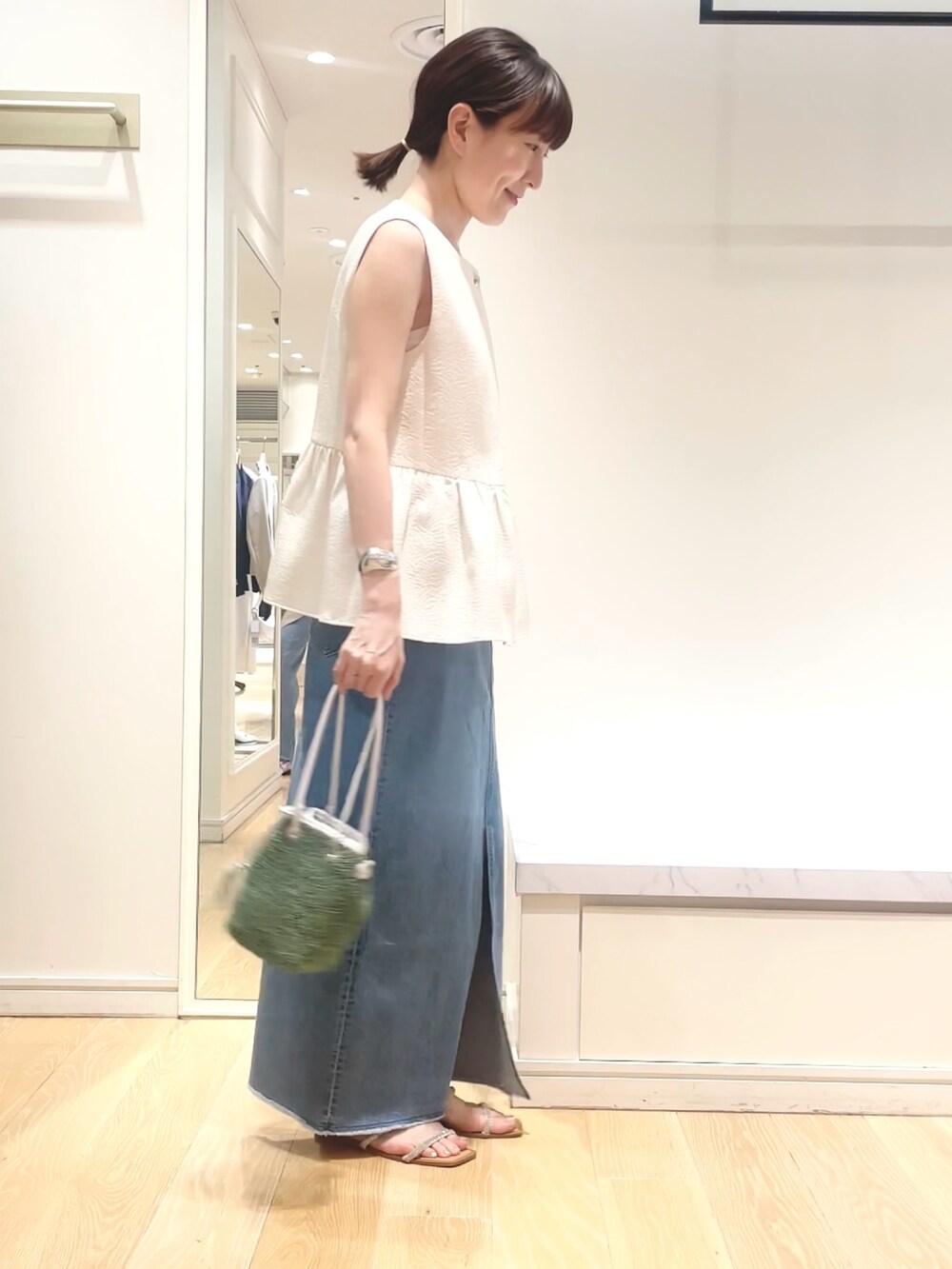 ホワイト系のベスト、グリーン系のショルダーバッグ、ブルー系のデニムスカートを着用したレディースの春コーディネートの8枚目の写真