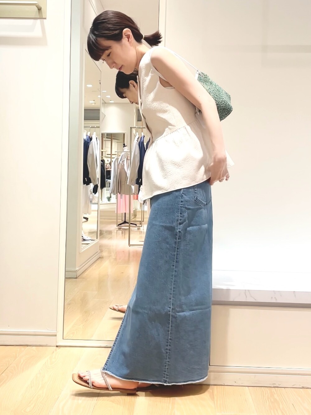 ホワイト系のベスト、グリーン系のショルダーバッグ、ブルー系のデニムスカートを着用したレディースの春コーディネートの2枚目の写真