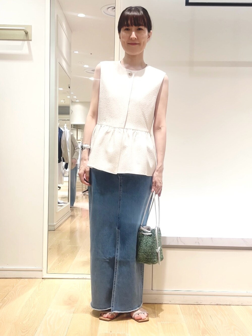 ホワイト系のベスト、グリーン系のショルダーバッグ、ブルー系のデニムスカートを着用したレディースの春コーディネートの4枚目の写真