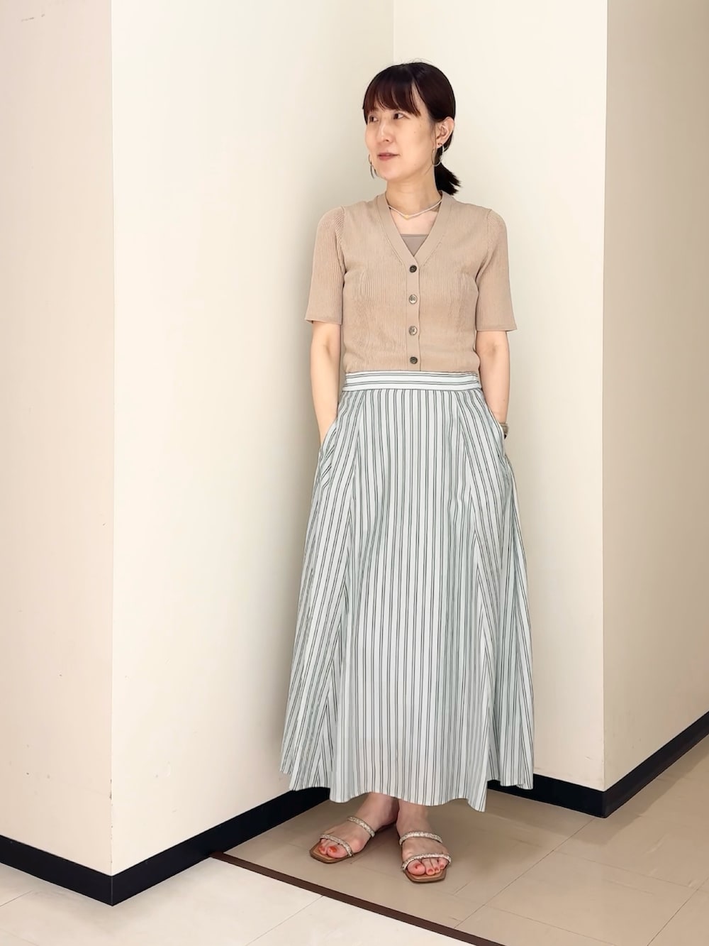 ブルー系のスカート、ベージュ系のカーディガン/ボレロ、ベージュ系のタンクトップを着用したレディースの夏コーディネートの2枚目の写真