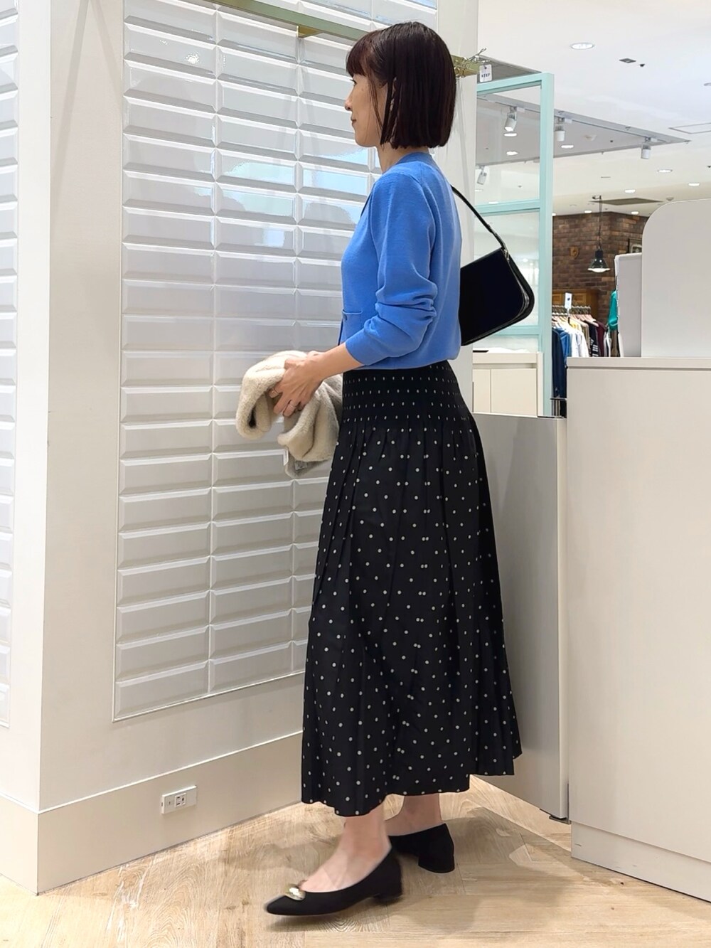 ブラック系のショルダーバッグ、ブルー系のカーディガン/ボレロ、ブラック系のスカートを着用したレディースの秋コーディネートの4枚目の写真