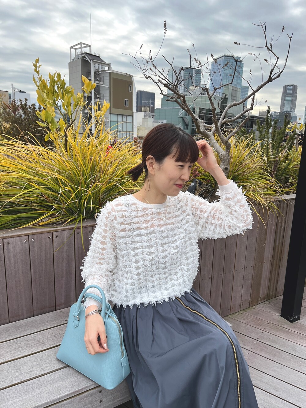 ブルー系のボストンバッグ、ブラック系のパンプス、グレー系のスカートを着用したレディースの冬コーディネートの8枚目の写真