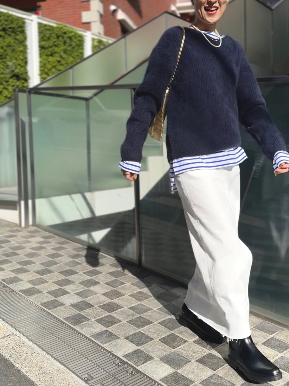 ゴールド系のクラッチバッグ、ブラック系のブーツ、ホワイト系のデニムスカートを着用したレディースの冬コーディネートの7枚目の写真