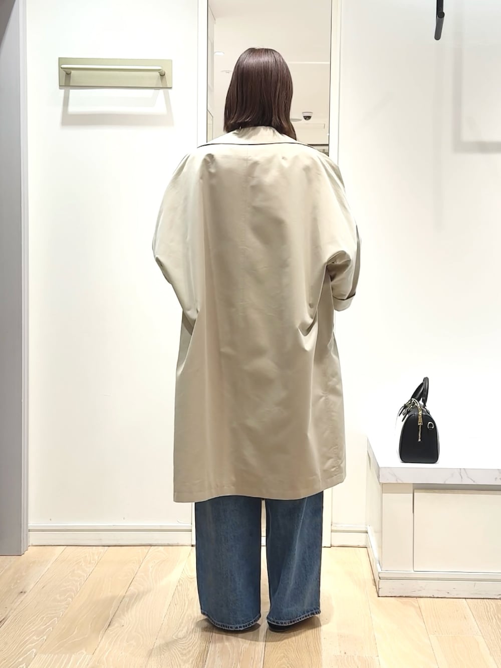 ブラック系のボストンバッグ、ブルー系のニット/セーター、ベージュ系のトレンチコートを着用したレディースの春コーディネートの4枚目の写真