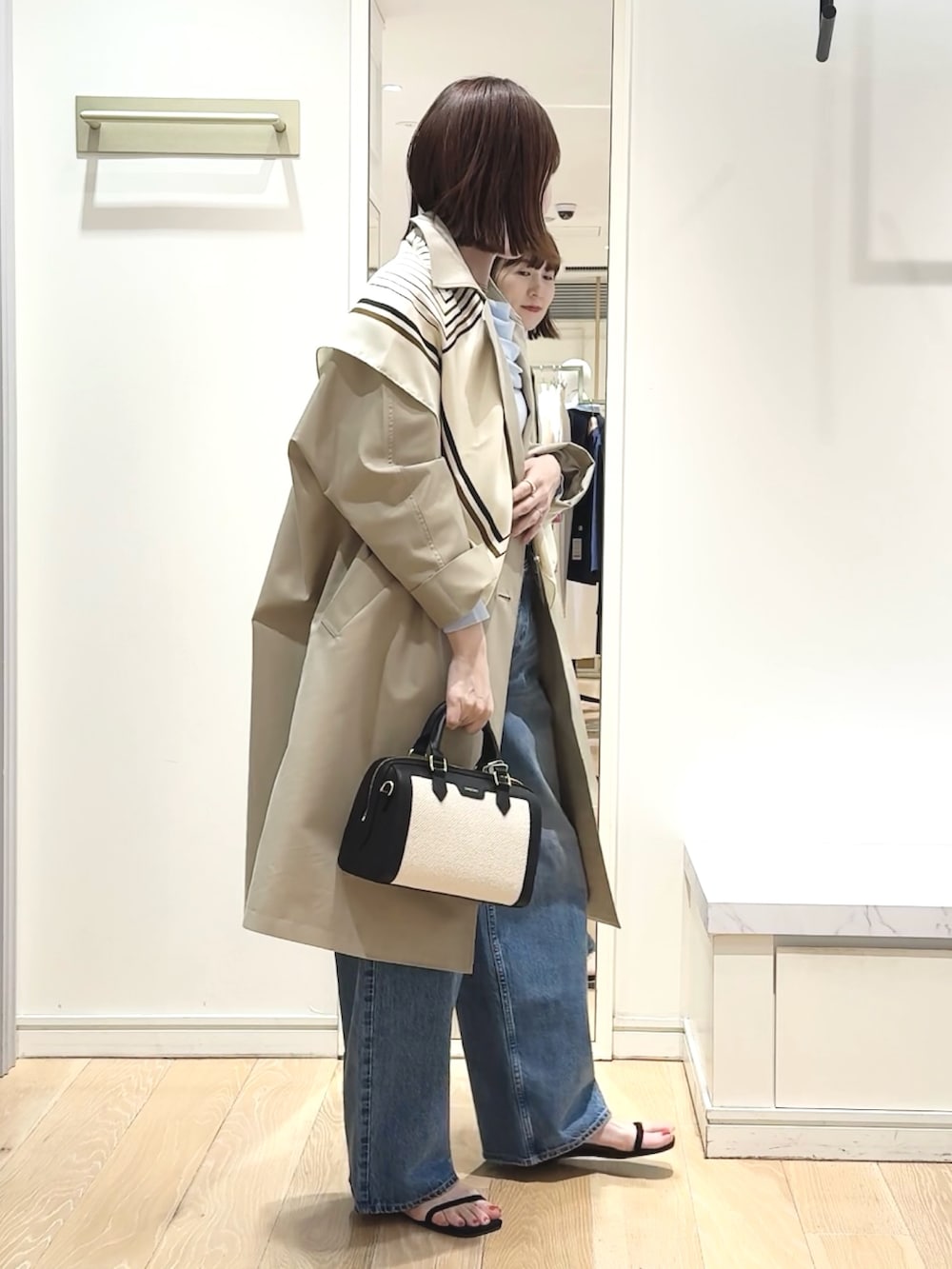 ブラック系のボストンバッグ、ブルー系のニット/セーター、ベージュ系のトレンチコートを着用したレディースの春コーディネートの5枚目の写真