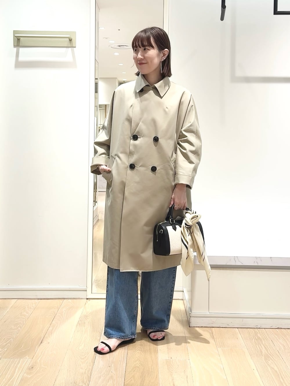 ブラック系のボストンバッグ、ブルー系のニット/セーター、ベージュ系のトレンチコートを着用したレディースの春コーディネートの7枚目の写真