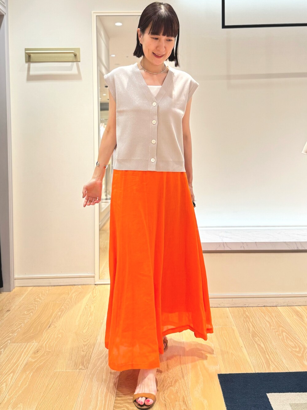 ベージュ系のベスト、ホワイト系のタンクトップ、オレンジ系のスカートを着用したレディースの夏コーディネートの7枚目の写真